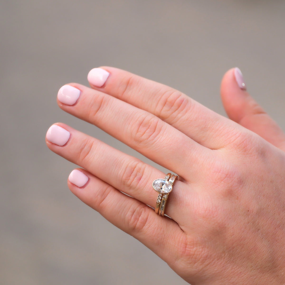 Hand wearing an oval engagement ring with a diamond wedding band